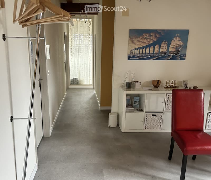 Hallway with a coat rack, a small white cabinet with books and decorative items, a red leather chair, and a painting on the wall.