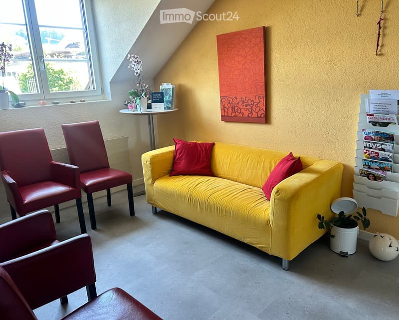 Bright living room with yellow sofa, red chairs, small round table, magazine rack, and artwork on the wall.