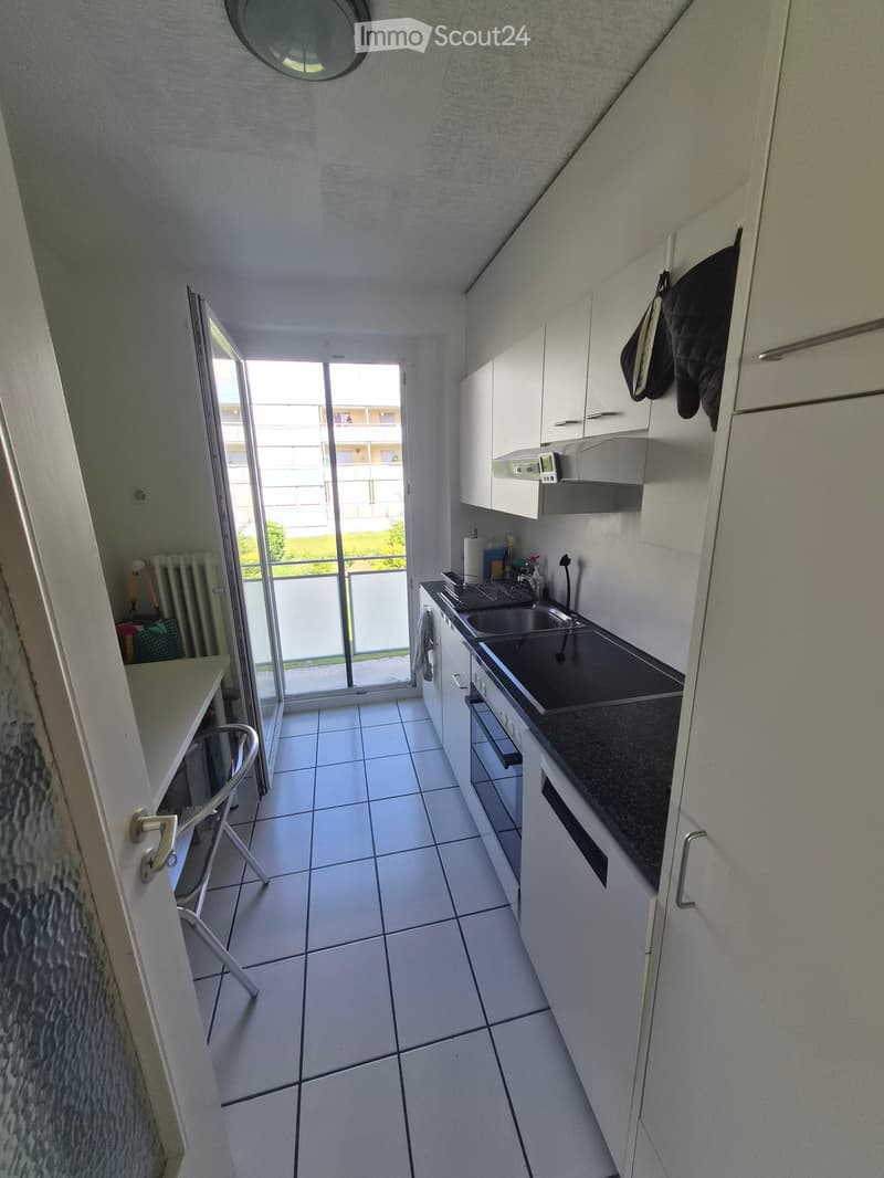 Modern kitchen with white cabinets, black countertop, sink, and a sliding glass door leading to a balcony.