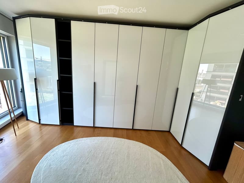 Empty room with wooden flooring, large mirrored sliding wardrobes, and large windows offering a city view.
