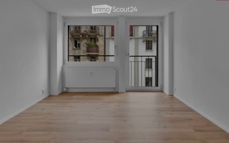 Empty room with wooden flooring, large window with balcony access, radiator, and white walls.