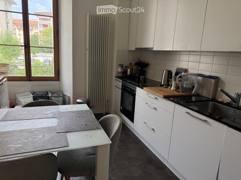 Modern kitchen with white cabinets, a central island, a dining table with two chairs, and various appliances including an oven, sink, and coffee maker.