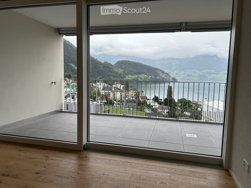 Balcony with large glass sliding doors, tiled floor, metal railing, overlooking a scenic lake and mountain landscape.