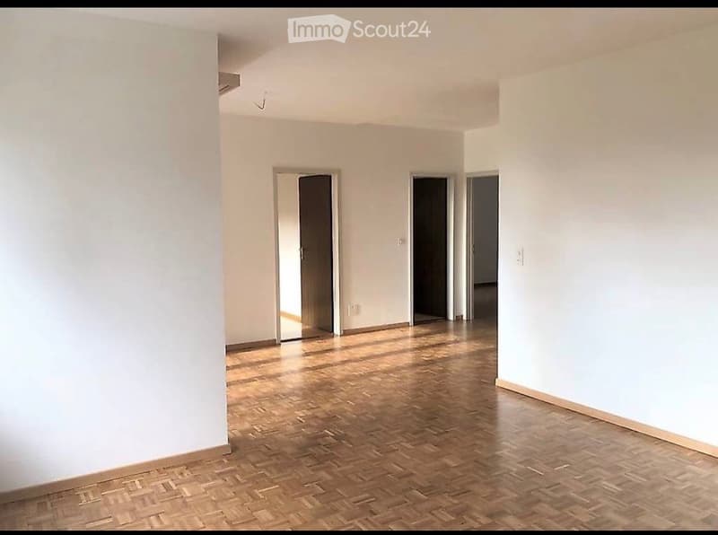 Empty room with wooden flooring and white walls, featuring three doorways leading to other spaces.