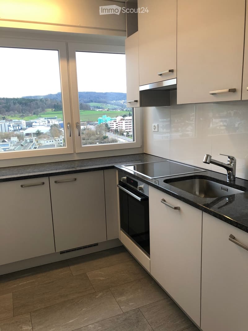 Modern kitchen with white cabinets, dark countertops, stainless steel sink, and built-in oven and microwave. Large windows offer a scenic view.