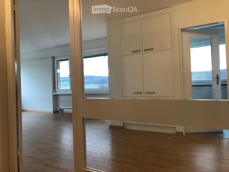 Empty room with wooden flooring, white walls, large windows, and built-in cabinets.