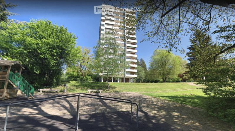 A park area with a playground, benches, and a multi-story residential building in the background.