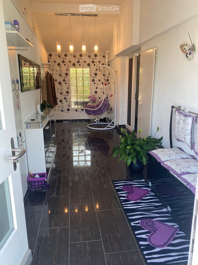 A modern hallway with dark tiled flooring, a purple hanging chair, a small table with a plant, a mirror, and a decorative rug with a heart design.