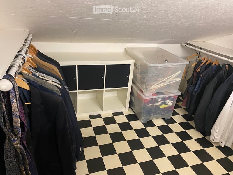 Well-organized walk-in closet with black and white checkered flooring, white built-in wardrobe with multiple compartments, and several hanging clothes and storage boxes.