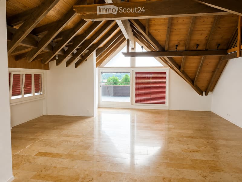 Bright, open room with wooden ceiling beams, large windows, and light-colored tile flooring. No furniture or furnishings are present.