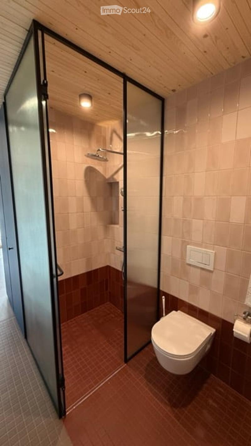 Modern bathroom with a glass-enclosed shower, toilet, and warm-toned tiles.
