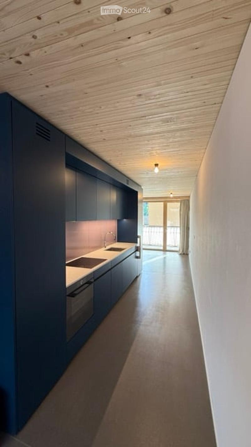 Modern kitchen with dark blue cabinets, white countertops, and a sleek design. Features a sink, faucet, and built-in oven. The space has a clean, minimalist aesthetic with a view to a balcony through large glass doors.