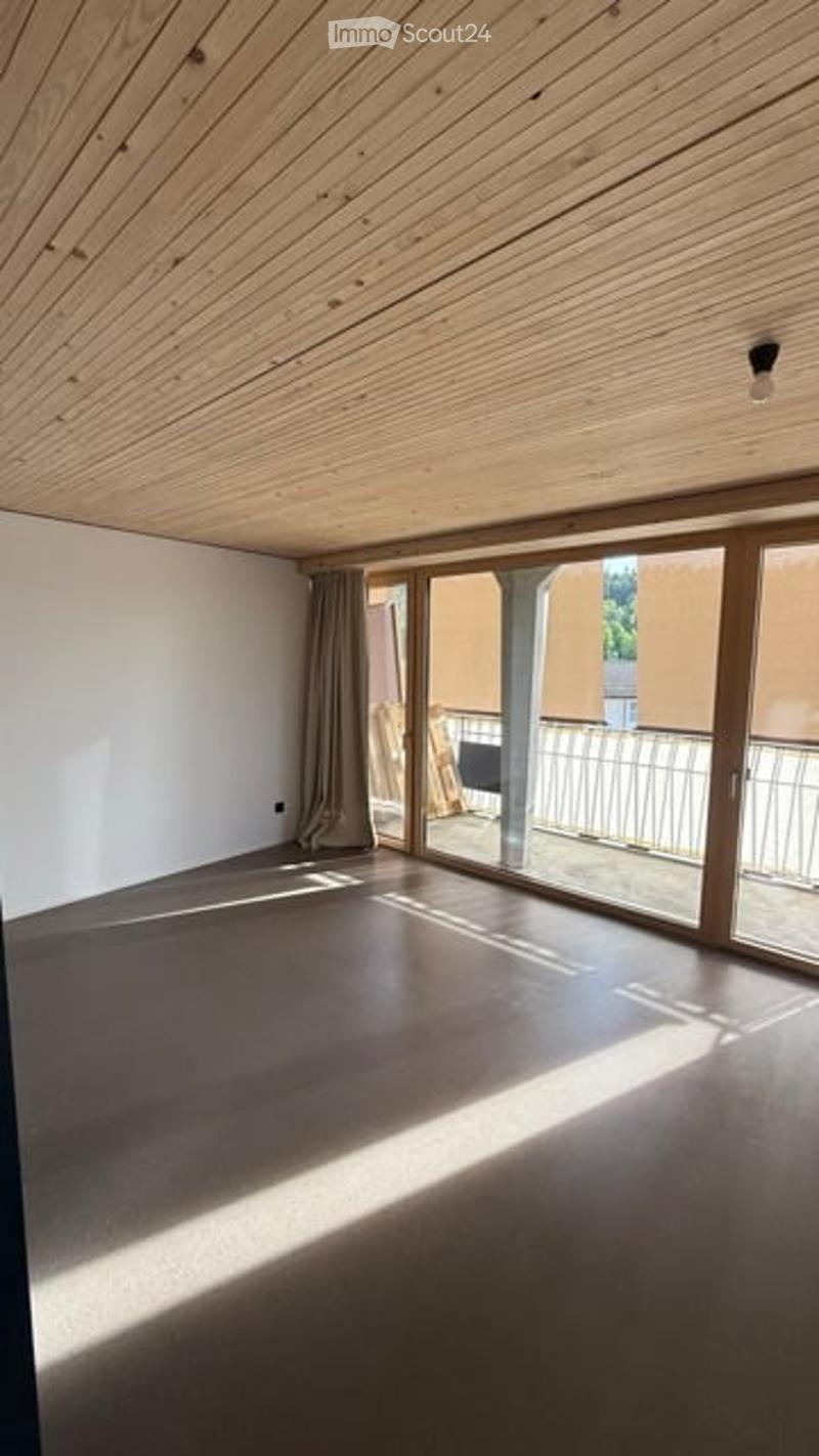 Empty room with wooden ceiling, large sliding glass doors leading to a balcony, and grey concrete floor.