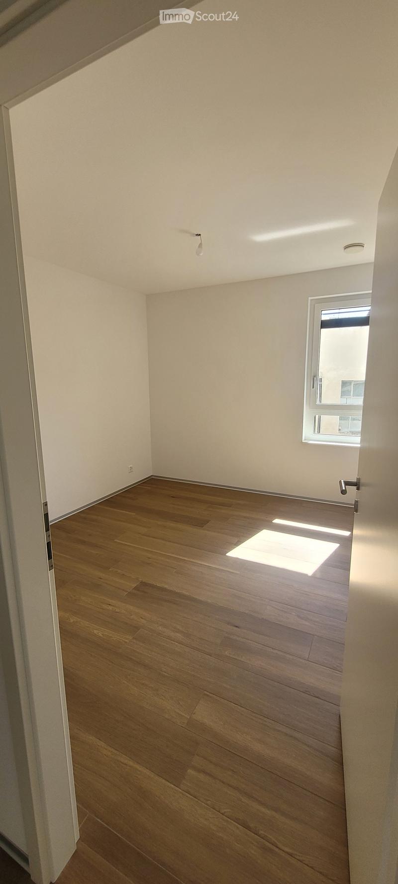 Empty room with wooden flooring, white walls, and a window letting in natural light. No furniture or equipment is present.