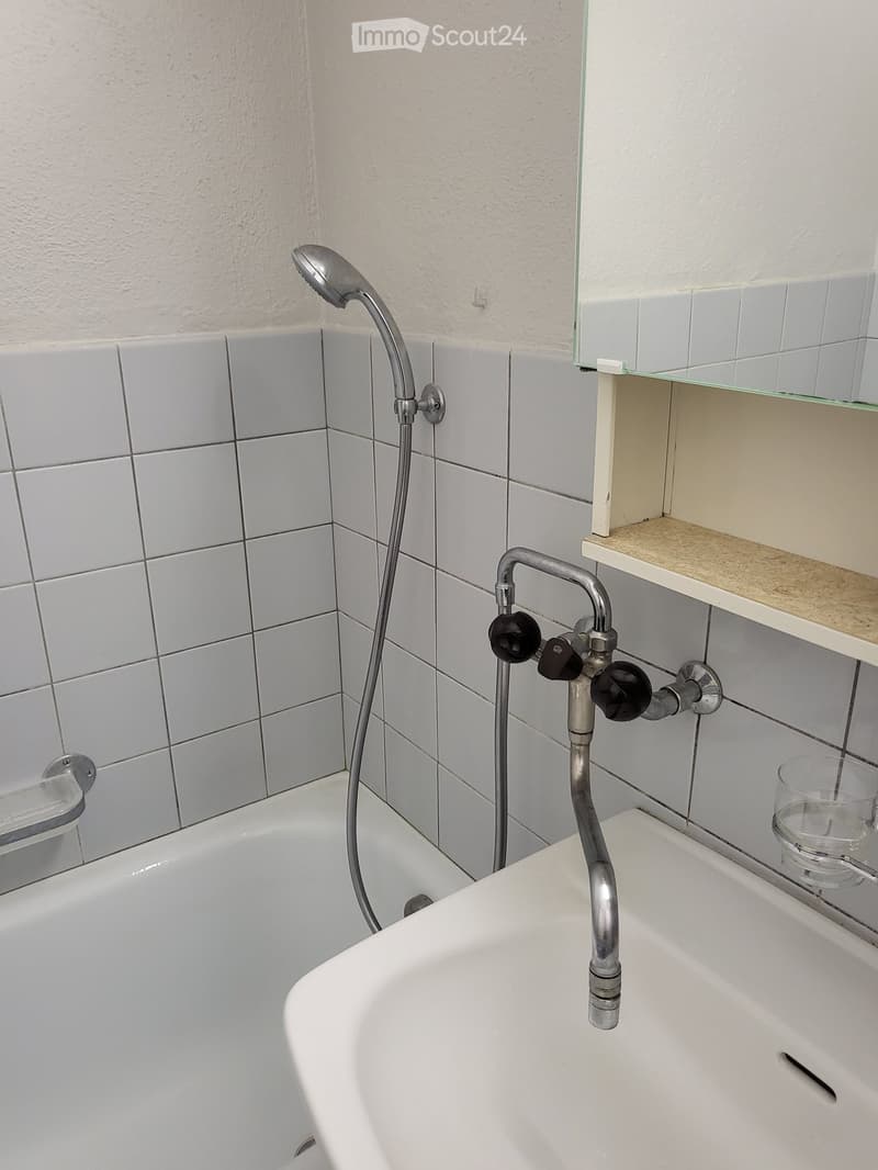 Bathroom with a bathtub, showerhead, faucet, and a small shelf with a glass container.