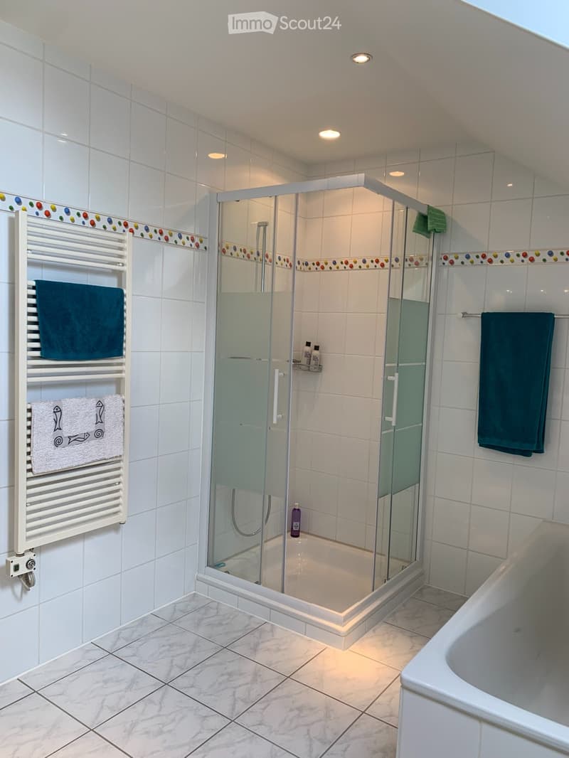 Modern bathroom with white tiled walls, marble flooring, a glass-enclosed shower, a bathtub, and a towel rack with towels.