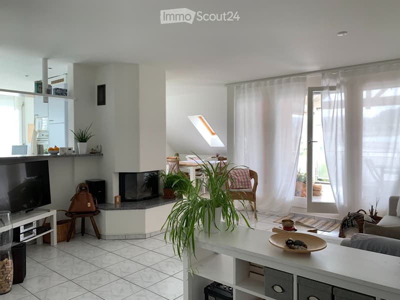 Bright living room with white walls, tiled floor, large windows with white curtains, fireplace, sofa, coffee table, TV, and plants.