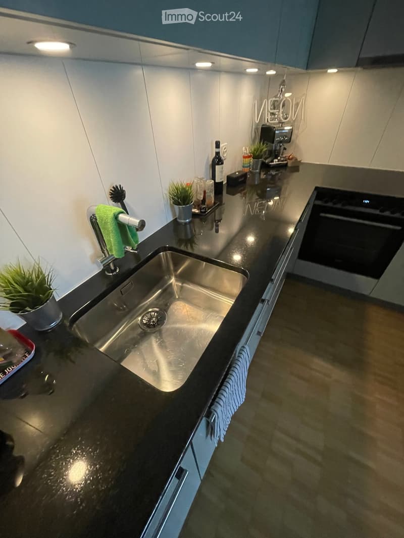 Modern kitchen with stainless steel sink, black countertops, built-in oven, and various small appliances and decorative items on the counter.