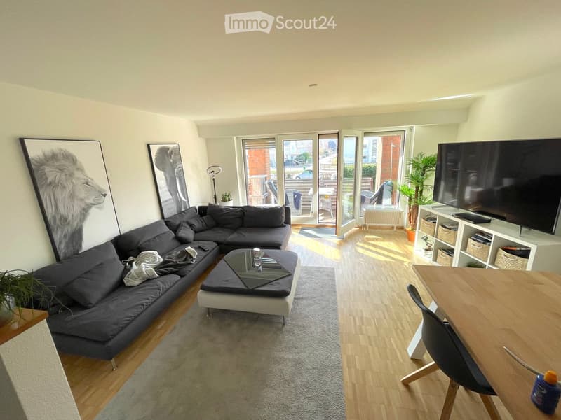 Modern living room with a grey sectional sofa, coffee table, dining table with chairs, TV, floor lamp, and artwork on the walls.
