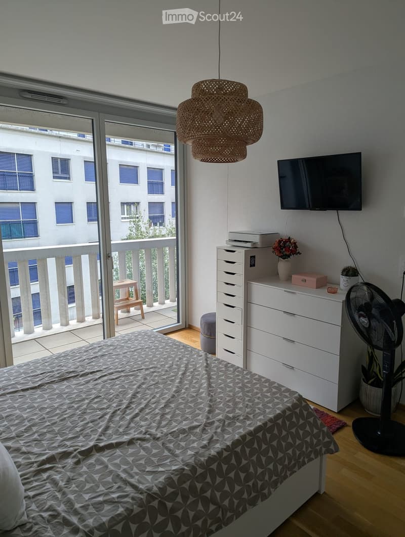 Modern bedroom with a bed, nightstand, fan, and a balcony with a small stool and table.