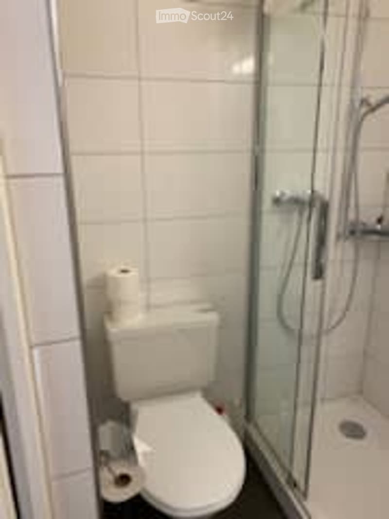 Modern bathroom with white tiles, a toilet, a glass-enclosed shower, and toilet paper on a holder.