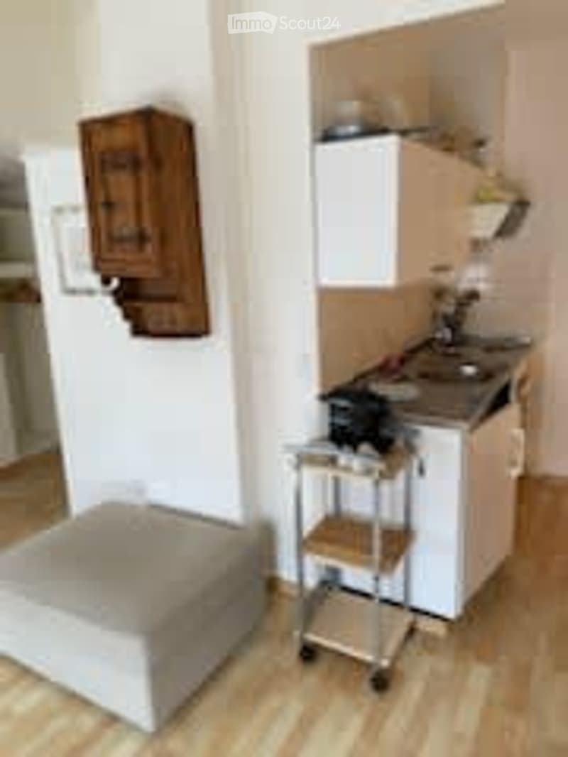 Small kitchen area with a stool, sink, and a cart. The space includes a kitchen cabinet and a faucet.