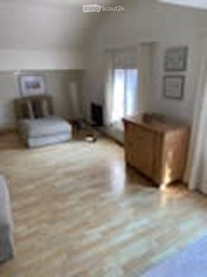 Bright living room with light wooden flooring, white walls, large window with blinds, a white sofa, a wooden chair, and a small table with picture frames on the wall.