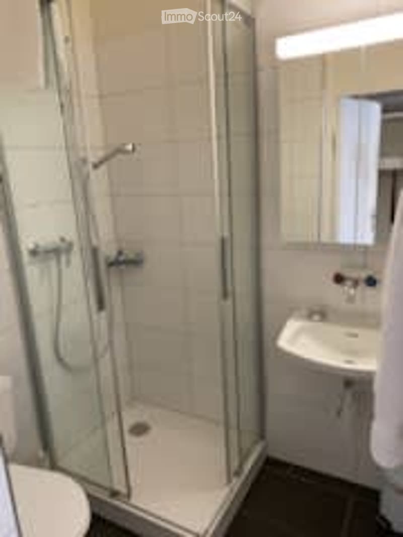 Modern bathroom with white tiles, glass-enclosed shower, toilet, sink, and mirror.