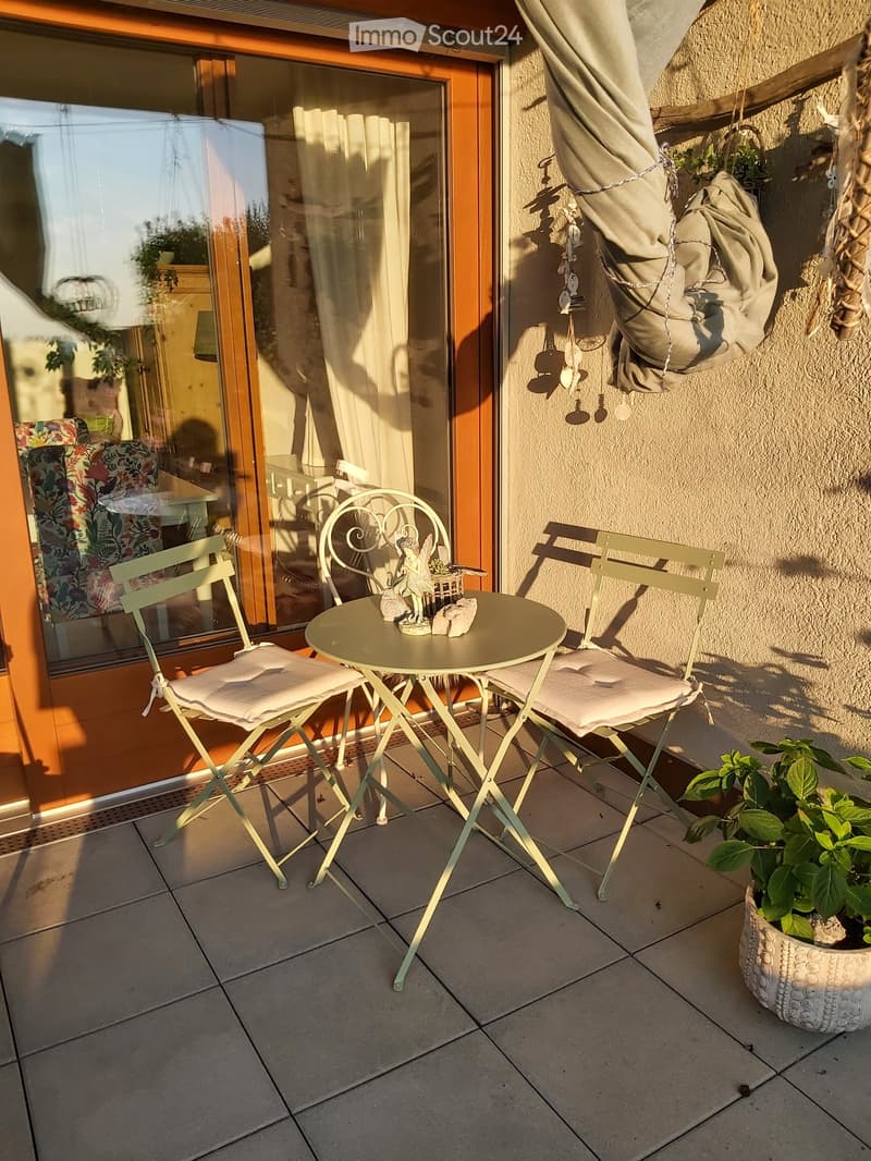 Balcony with a small round table, two chairs, a decorative statue, and a potted plant. The balcony has tiled flooring and is adjacent to a glass door leading inside.