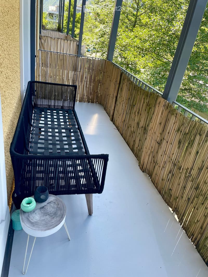 Balcony with a black woven chair, a round white table, and a cup on the table. Bamboo privacy screen on the right side.