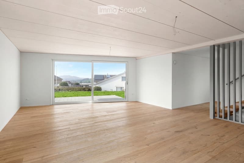 Empty room with light wooden flooring, white walls, and large glass doors leading to a view of a green lawn and distant houses.