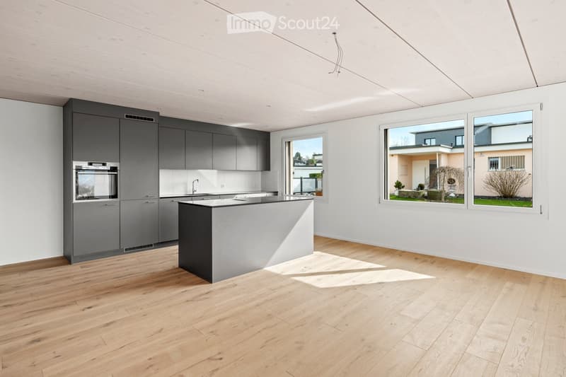 Modern kitchen with grey cabinets, a central island, and large windows overlooking a garden area.