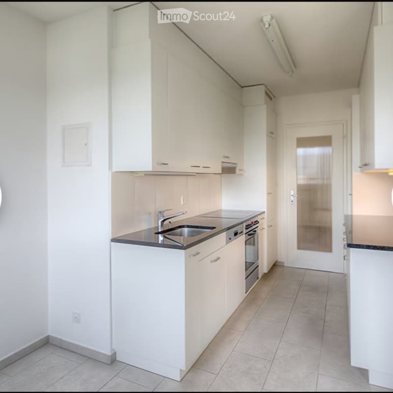 Modern kitchen with white cabinets, a black countertop, a sink, and an oven. The space is clean and well-lit with tiled flooring.