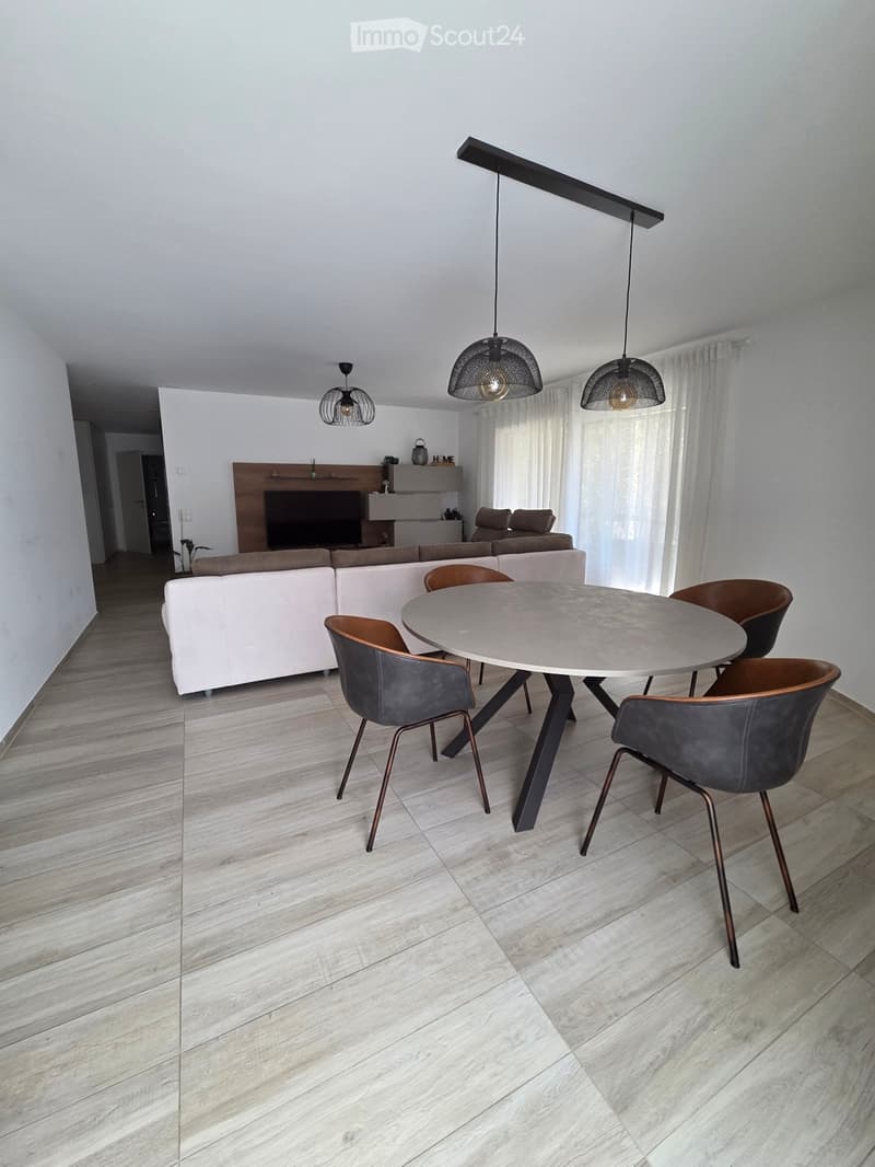 Modern living and dining area with white walls, light wood flooring, a white sectional sofa, a round dining table with four chairs, and a fireplace with a TV above it.
