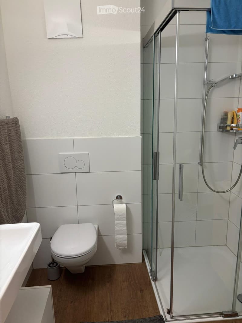 Modern bathroom with white tiles, a bathtub, toilet, glass-enclosed shower, and a towel on the wall.