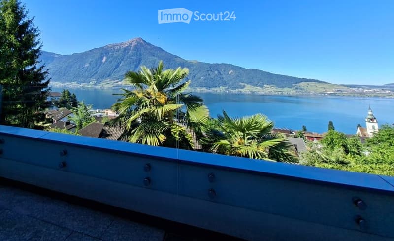 Balcony with a scenic view of a lake and mountains, surrounded by palm trees and greenery.