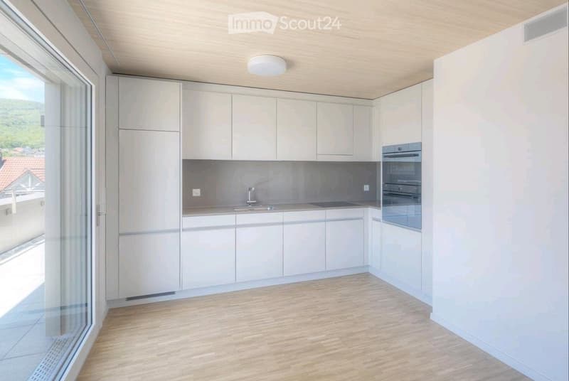 Modern kitchen with light-colored cabinets, a sink, and an oven. The space features wooden flooring and large windows offering a scenic view.