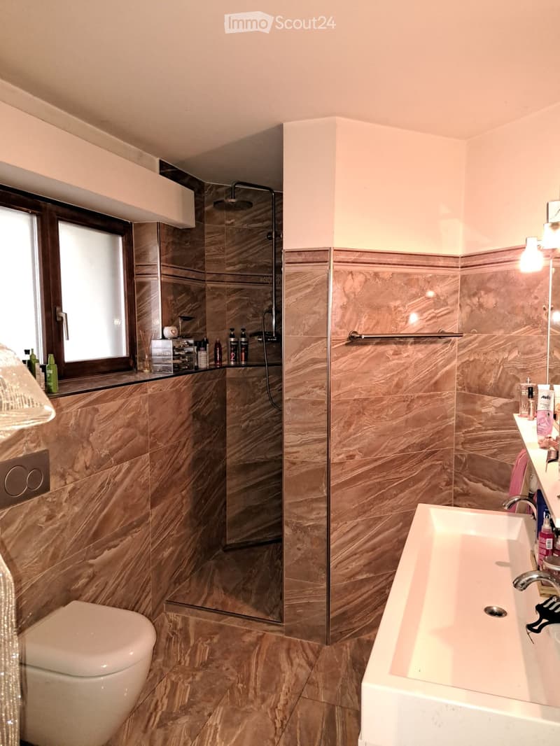 Modern bathroom with marble tiles, a bathtub, toilet, shower, and various toiletries on the counter.
