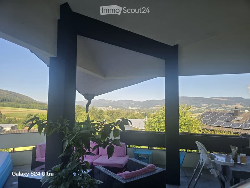 Balcony with a view of the countryside, featuring a pink sofa, wicker chairs, a small table, and a baby chair.