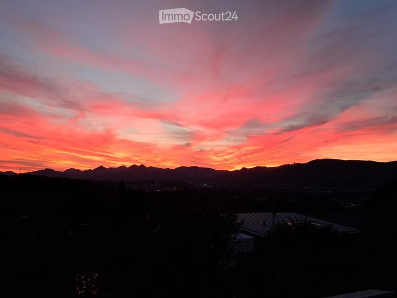 A scenic view of a sunset over a cityscape with mountains in the background, featuring vibrant pink and orange hues in the sky.