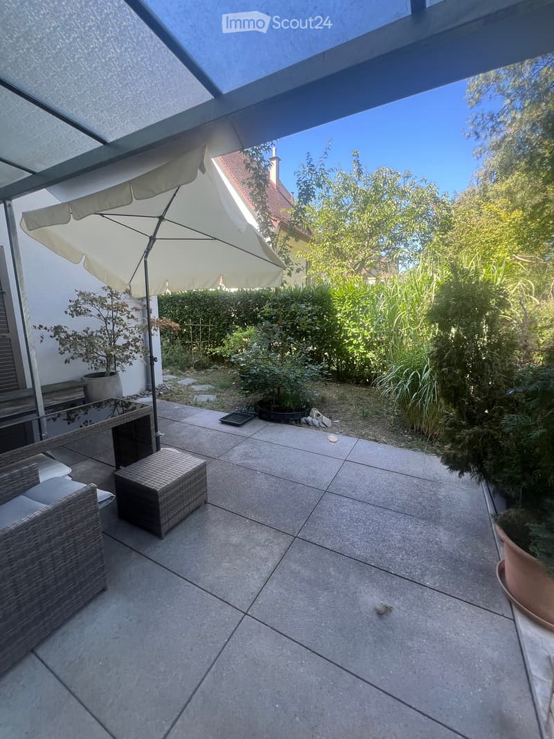 Patio with concrete tiles, wicker sofa, stool, umbrella, and potted plants.