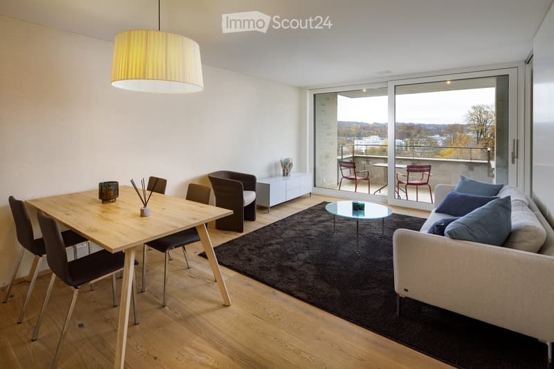 Modern living and dining area with a grey sofa, coffee table, dining table, chairs, side table, and a large window with a view of the city.