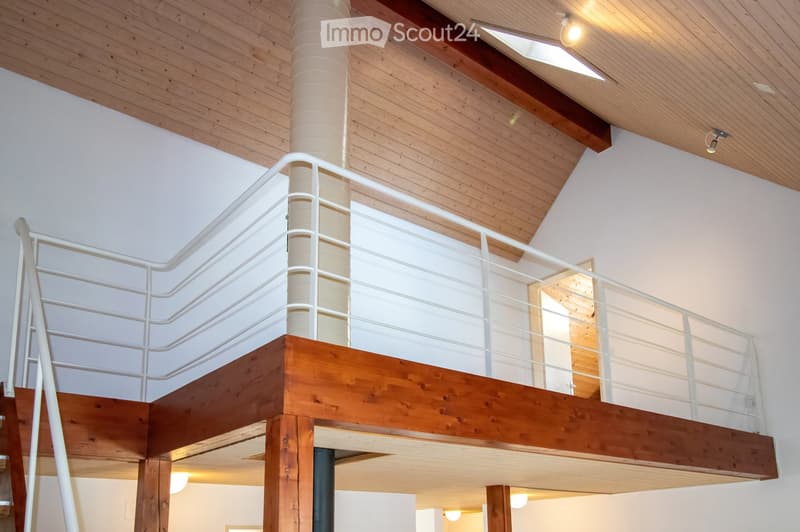 Modern interior with wooden ceiling, white walls, and a raised wooden platform with a white railing, creating a loft-style space.