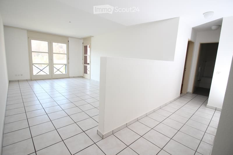 Empty room with white tiled flooring, white walls, and large windows with sliding doors leading to a balcony.