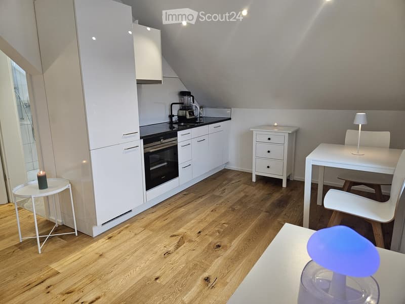 Modern kitchen with white cabinets, stainless steel appliances, wooden flooring, and a small dining area with a table and chairs.