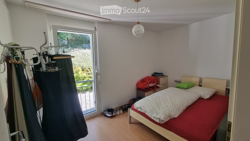 Cozy bedroom with a single bed, nightstand, backpack, shoe rack, and a hanging clothes rack near the window.