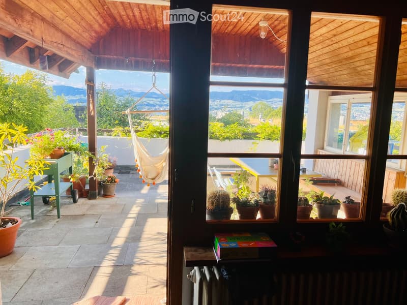 Balcony with wooden ceiling, potted plants, a hammock, and a view of the mountains.