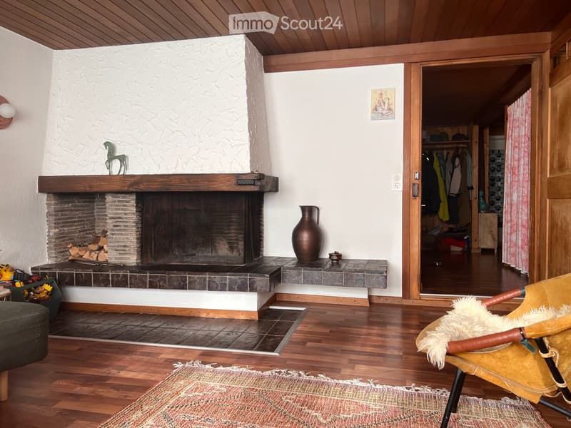 Living room with wooden floors, fireplace, sofa, chair, vase, sculpture, and picture frame.