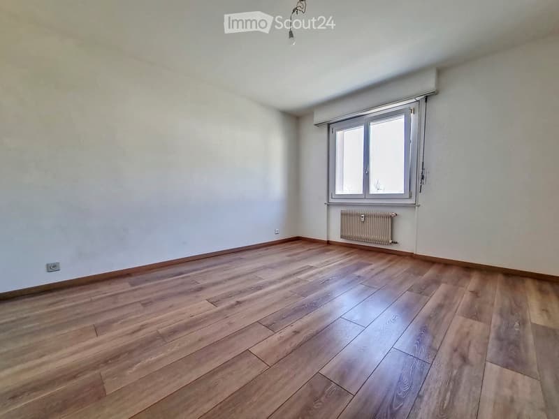 Empty room with wooden flooring, white walls, a window with blinds, and a radiator under the window.