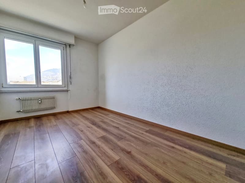 Empty room with wooden flooring, white walls, and large windows offering a view of the landscape.